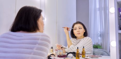 Beautiful middle aged woman doing makeup in front of a mirror